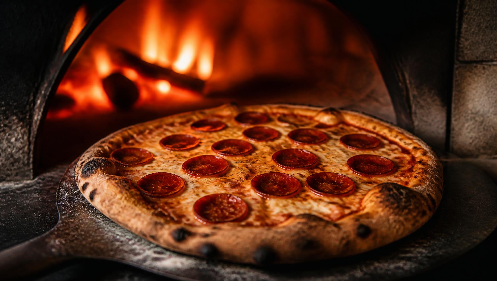 Wood-fired pepperoni pizza coming out of a stone oven